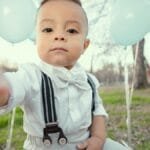 Cute toddler dressed formally with blue balloons, seated outdoors in Tulsa, Oklahoma.