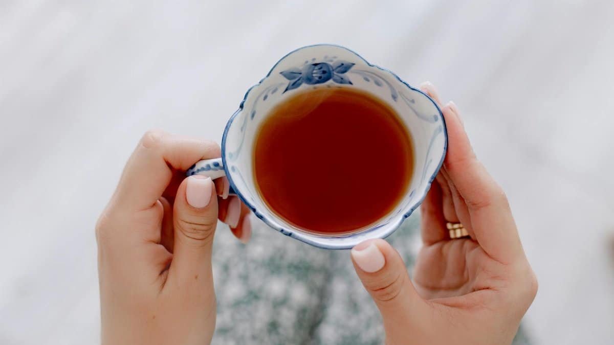 A detailed view of hands holding an ornate ceramic tea cup with warm tea indoors.