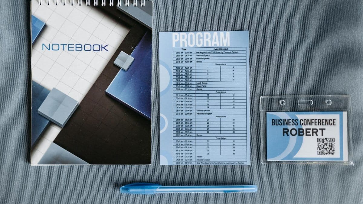 Flatlay of a notebook, conference badge, pen, and program on gray surface.