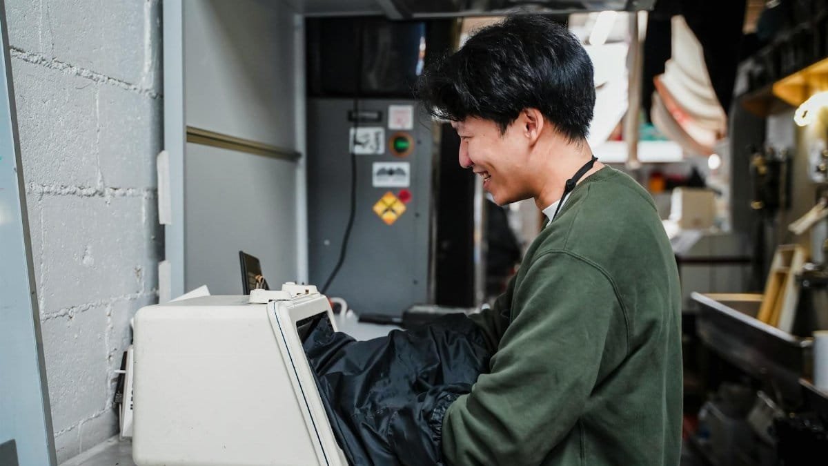 Young man smiling while operating industrial machinery in a factory setting.