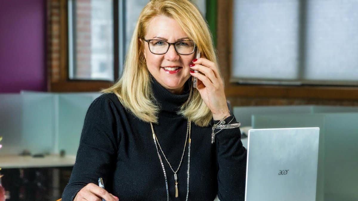 Smiling businesswoman on phone call, working on laptop in sleek office setting.