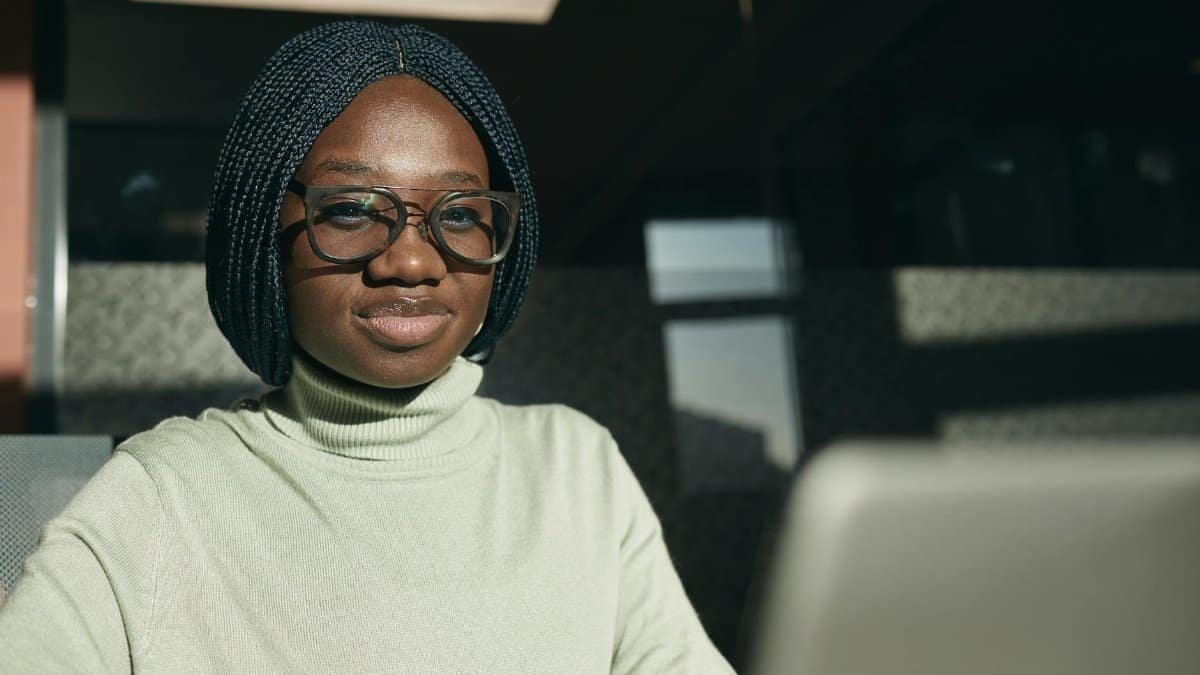 Confident woman with glasses and braided hair working at her laptop in a modern office setting.