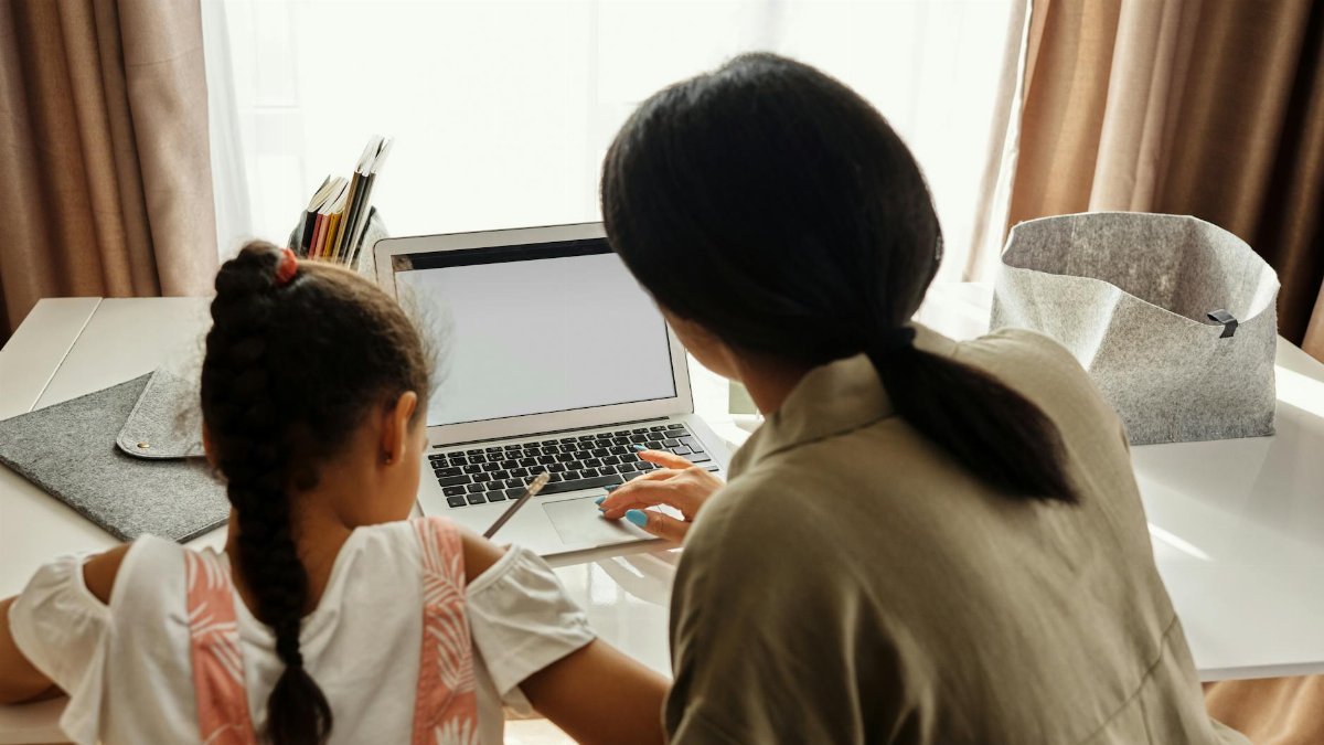 A mother helps her daughter with online learning on a laptop at home, emphasizing family education.
