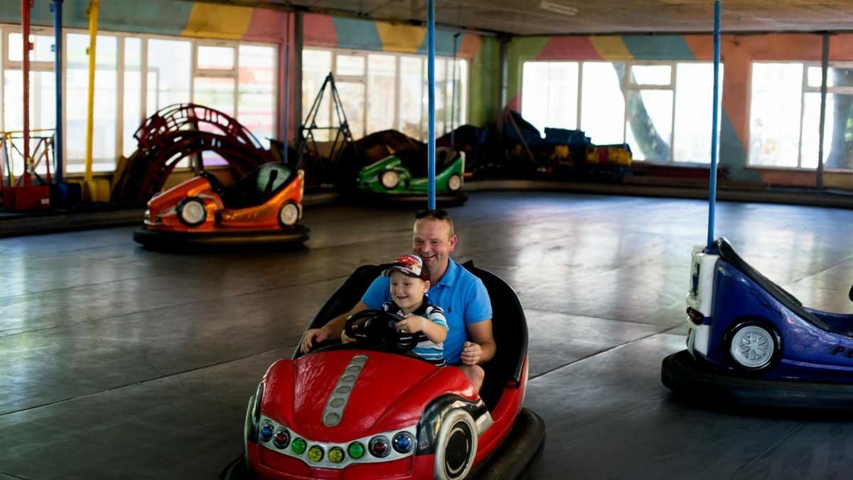 Playful moment of father and son driving a bumper car together indoors.