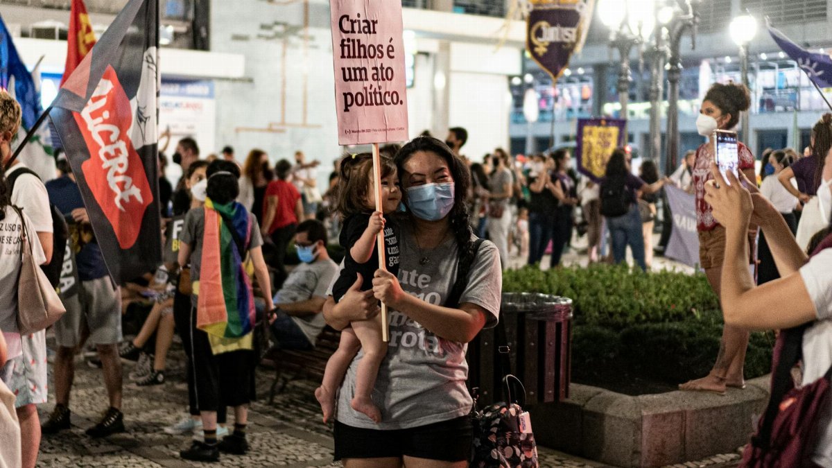 A mother and child at a protest holding a sign that translates to 'Raising children is a political act'.