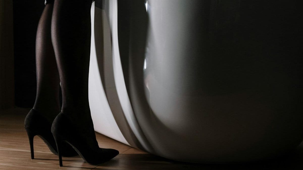 Close-up of high heels on a wooden flooring next to a sleek white bathtub.