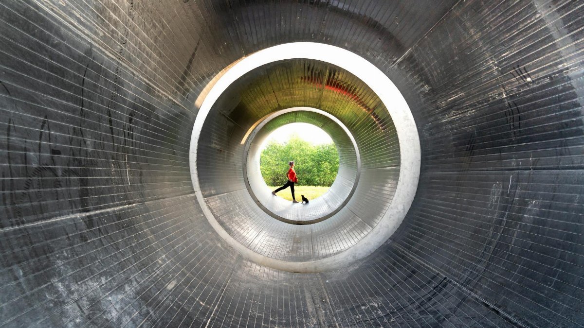 Person in a red shirt walking inside a large industrial metal tunnel with a circular perspective.