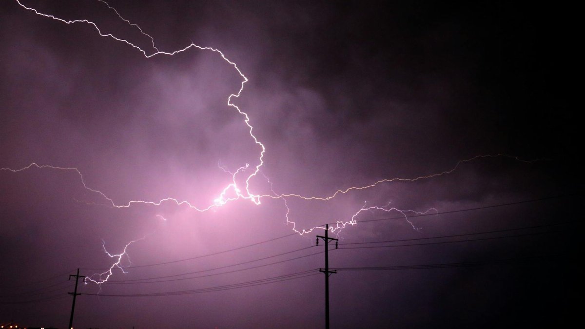 Stunning lightning bolts illuminate a stormy night sky over silhouetted power lines.