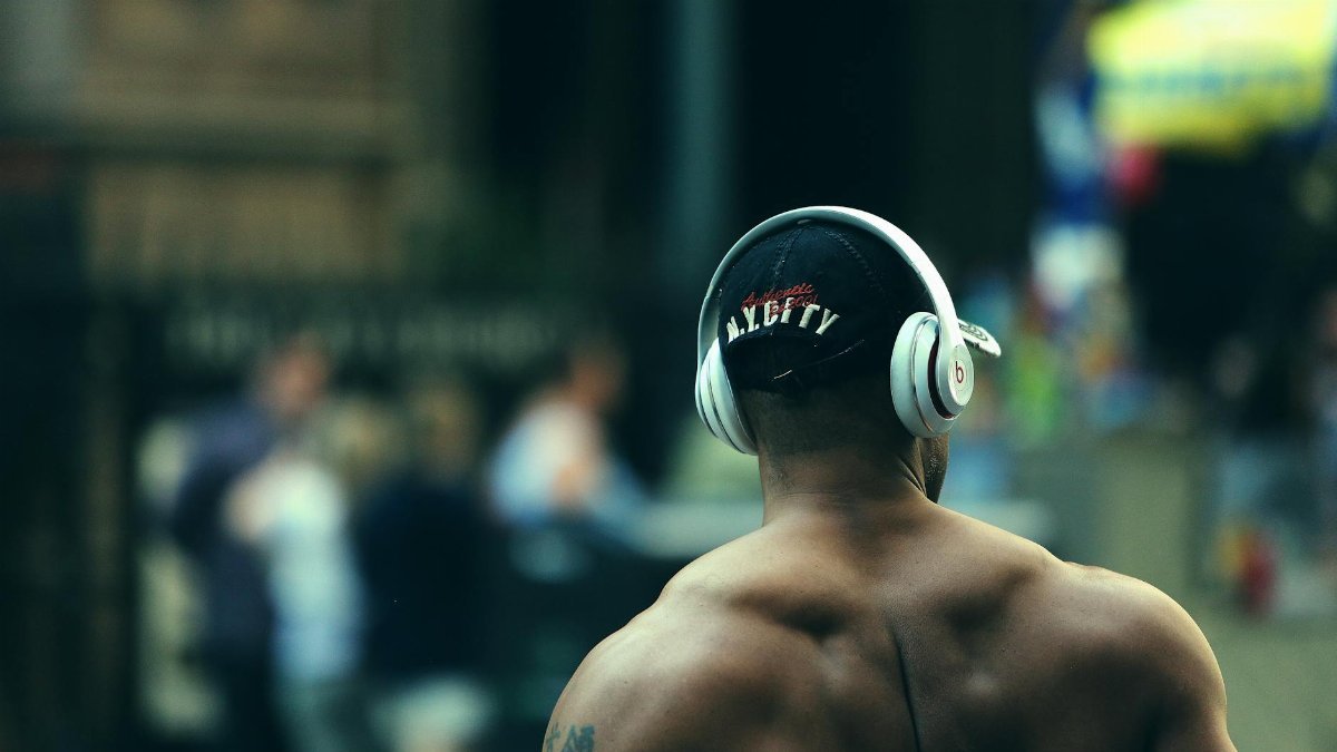 Fit man wearing headphones, enjoying music outdoors in a street setting.