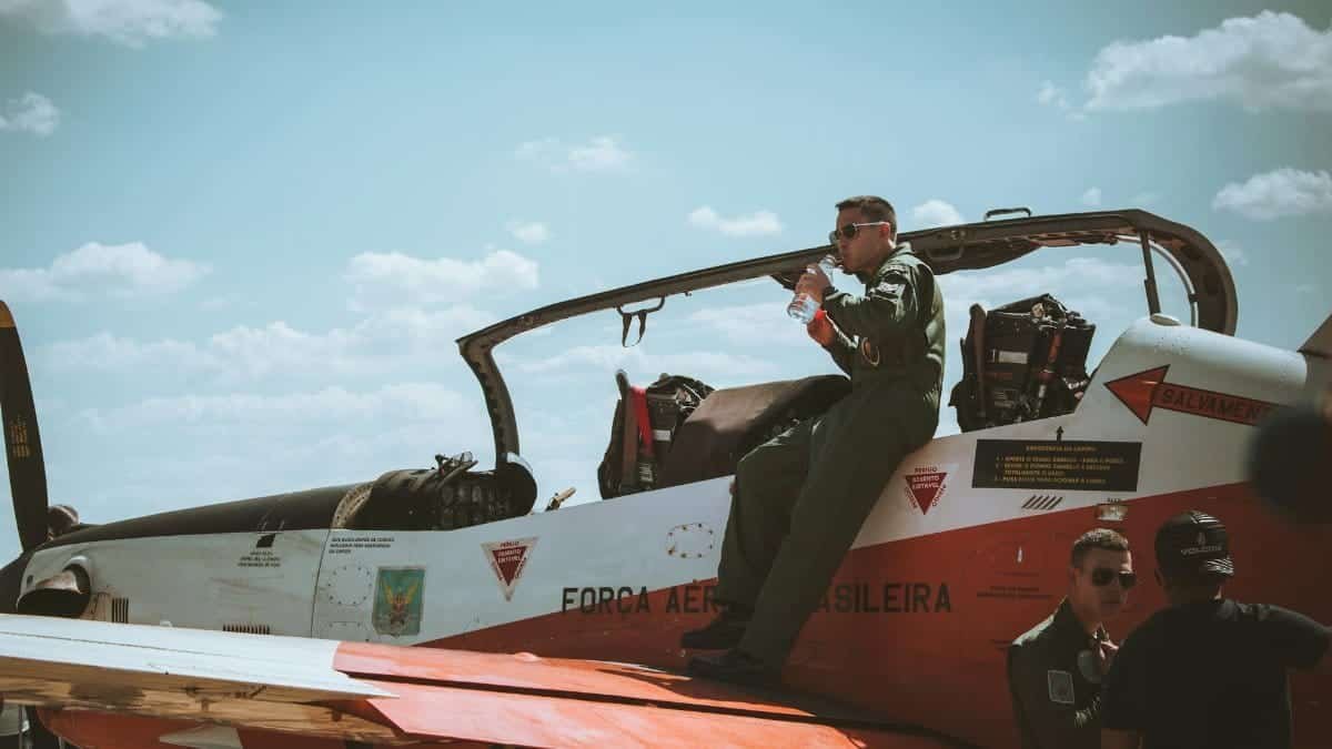 A Brazilian Air Force pilot resting on a fighter jet wing, illustrating aviation and military life.