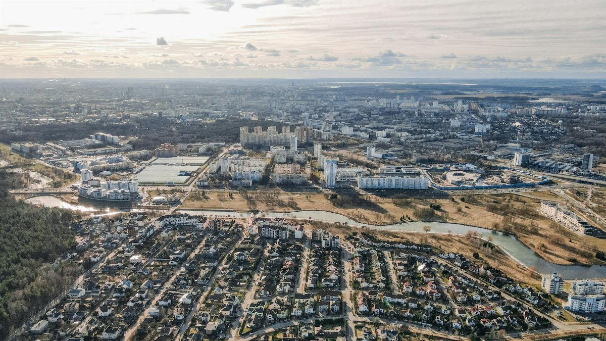 Aerial view of a sprawling cityscape with diverse architecture and a winding river under a cloudy sky.