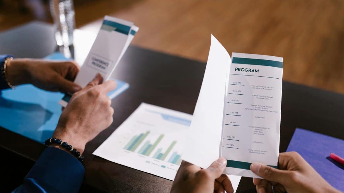 Hands examine program guide in a corporate meeting setting, highlighting agenda details.