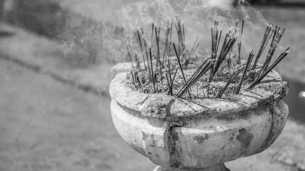 Black and white photo of incense sticks in a pot with smoke rising during a ritual.