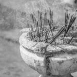 Black and white photo of incense sticks in a pot with smoke rising during a ritual.