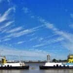 Twin ferries on a river with a vibrant city skyline and clear blue sky.