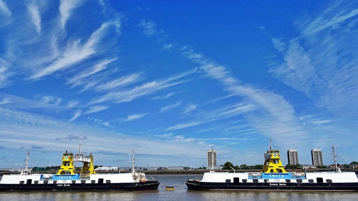 Twin ferries on a river with a vibrant city skyline and clear blue sky.