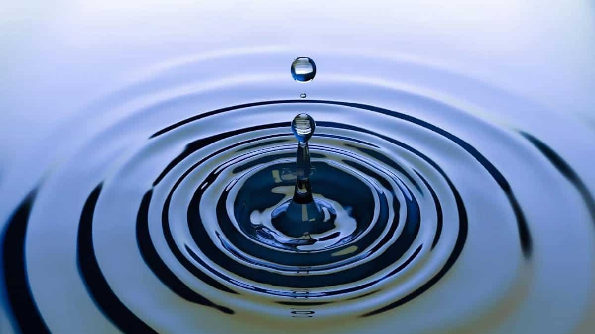 A stunning close-up of a water droplet creating ripples on a smooth water surface, capturing nature's simplicity.