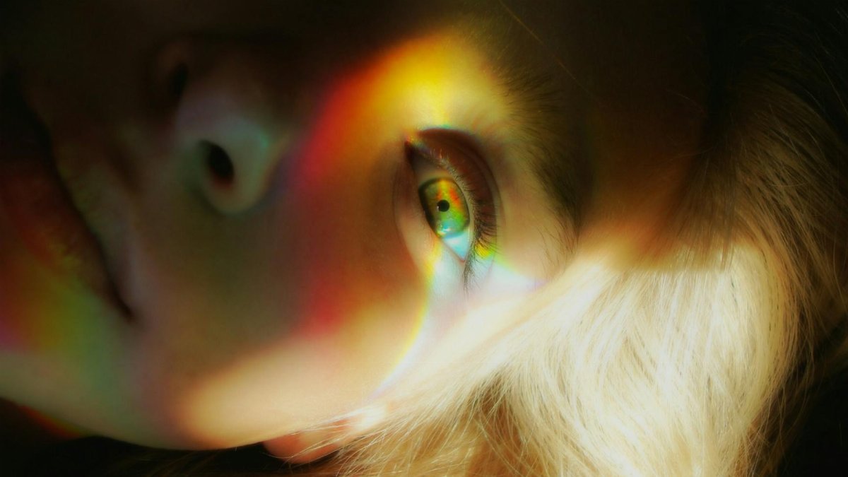 Close-up portrait of a woman with rainbow light reflections creating a surreal effect.
