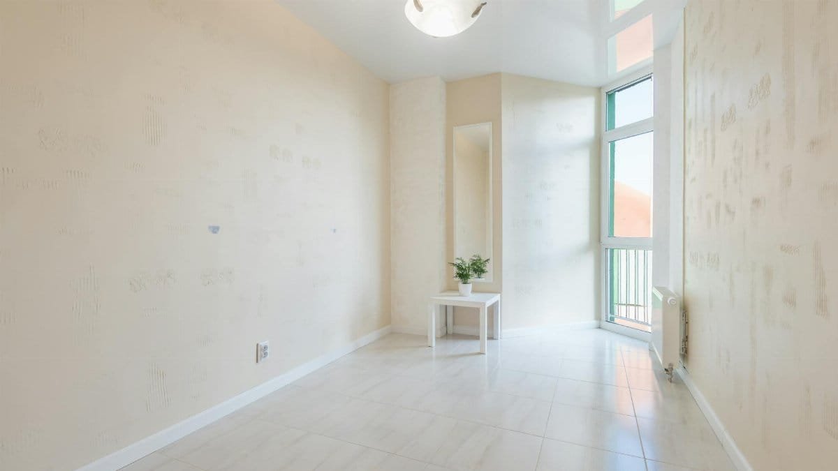 Empty room with tiled floor and potted plant on table near balcony door reflecting on stretch ceiling
