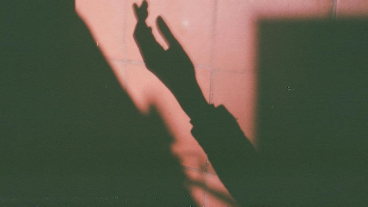 A shadow of a hand making a gesture on a red wall, casting an abstract and mysterious feel.
