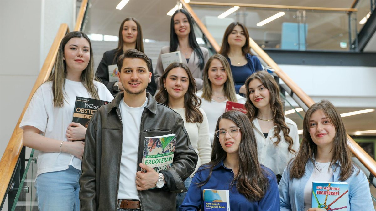 Diverse group of students smiling on stairs, holding educational books indoors.