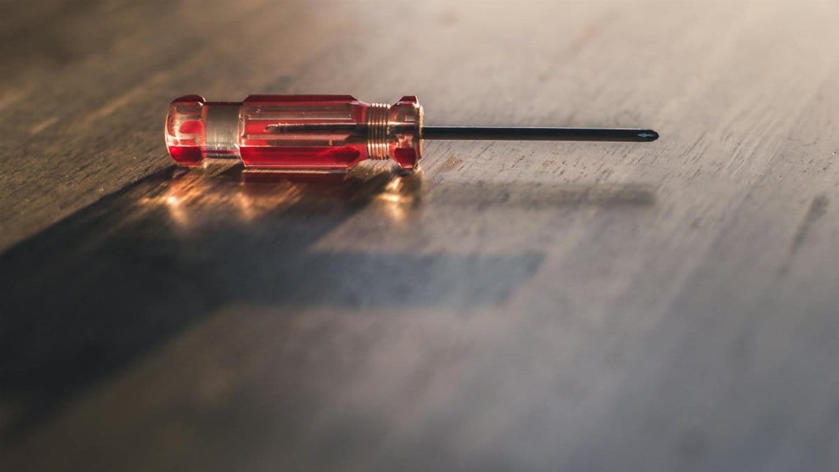 A red screwdriver lies on a wooden surface, highlighting its metallic and transparent handle.