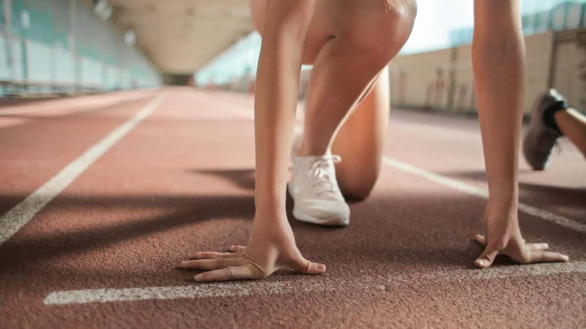 Focused female athlete in crouch start position preparing to sprint on an indoor track.