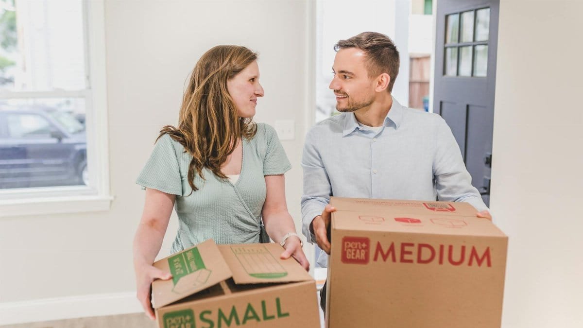 A smiling couple carries moving boxes into their new home, symbolizing a fresh start.