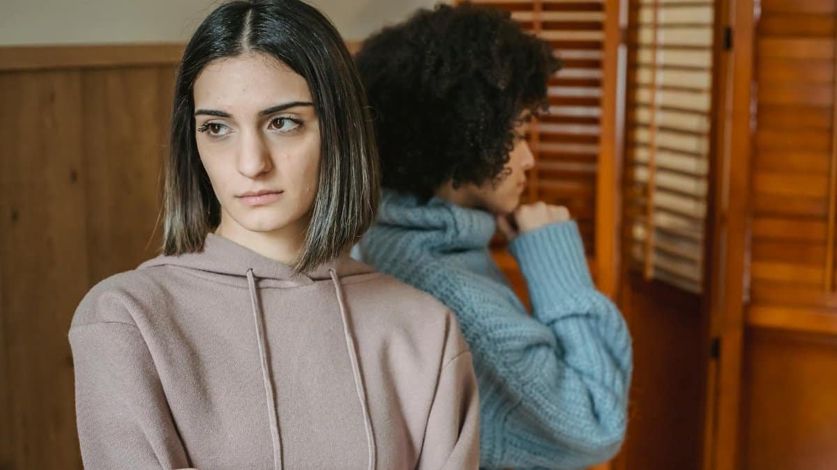 Upset multiracial women in casual wear standing in light room near wall with wooden folding screen while having conflict at home