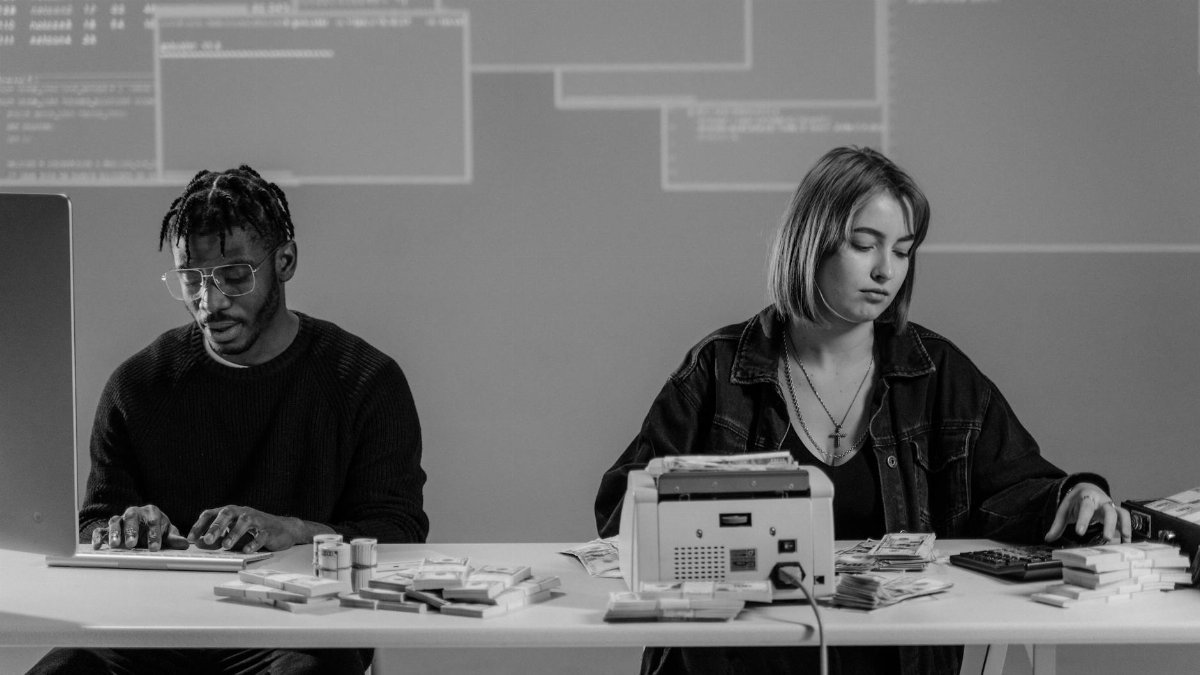 Two professionals working with computers and currency at a desk in a modern office setting.