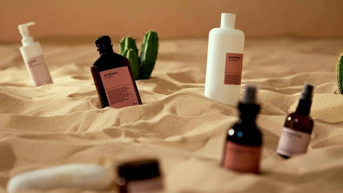 Cosmetic and skincare products artistically arranged on sand with cactus accents, evoking a desert vibe.