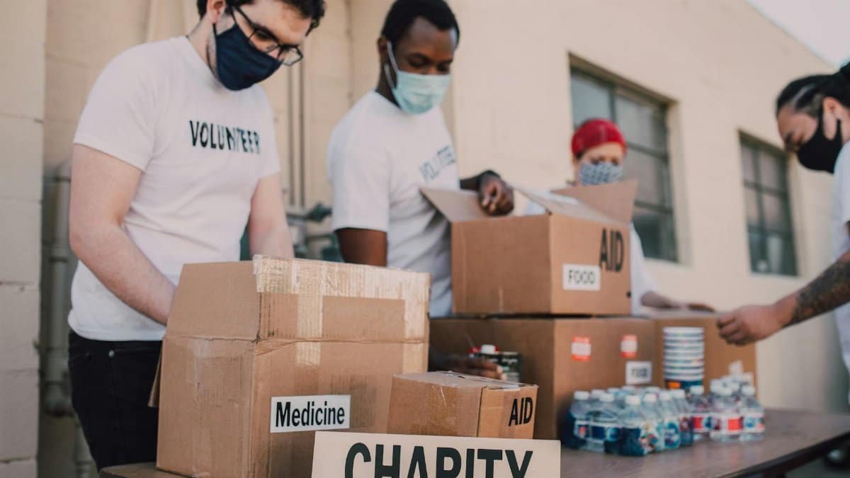 Group of volunteers wearing masks organizing donation boxes labeled food and medicine outdoors.