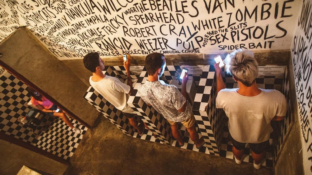 From above full length faceless people in casual clothes using mobile phones in public toilet with black and white tiles and inscriptions on walls gadget addiction concept