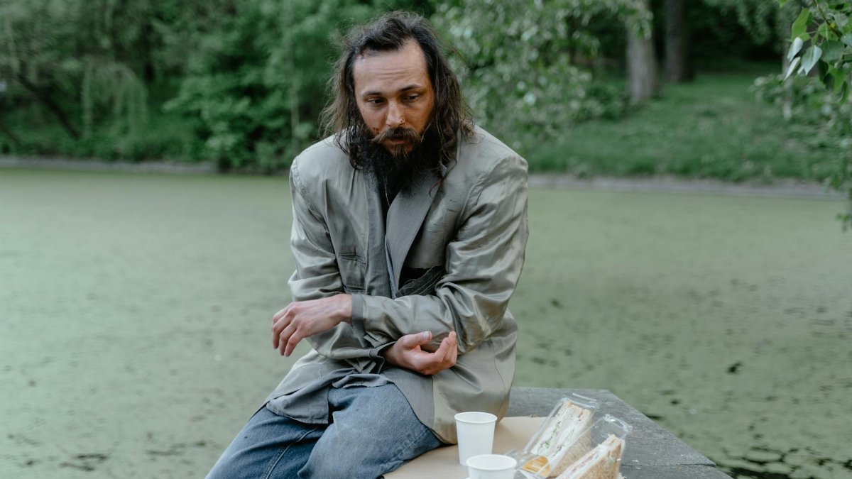 Elderly man sitting outdoors with sandwiches, reflecting in solitude.