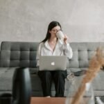 Woman sipping coffee while working on a laptop in a cozy home setting, highlighting remote work lifestyle.