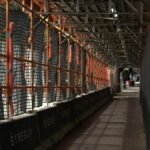 Pedestrian walkway through a construction site with safety signs and scaffolding overhead.