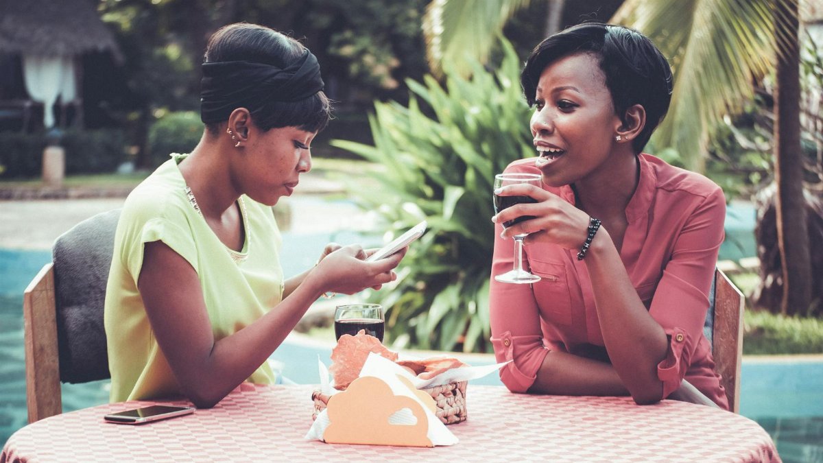 Two women enjoying a relaxing outdoor lunch by the pool, sipping drinks and chatting.