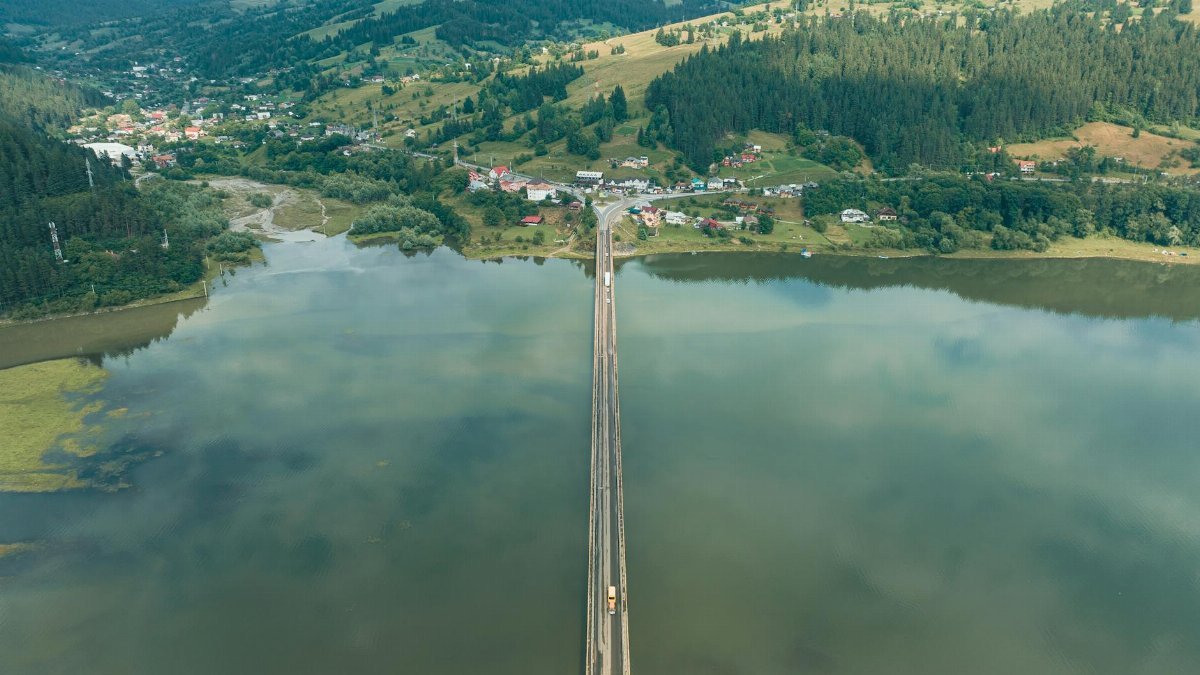 Drone view of a bridge crossing a serene lake with lush green surroundings.
