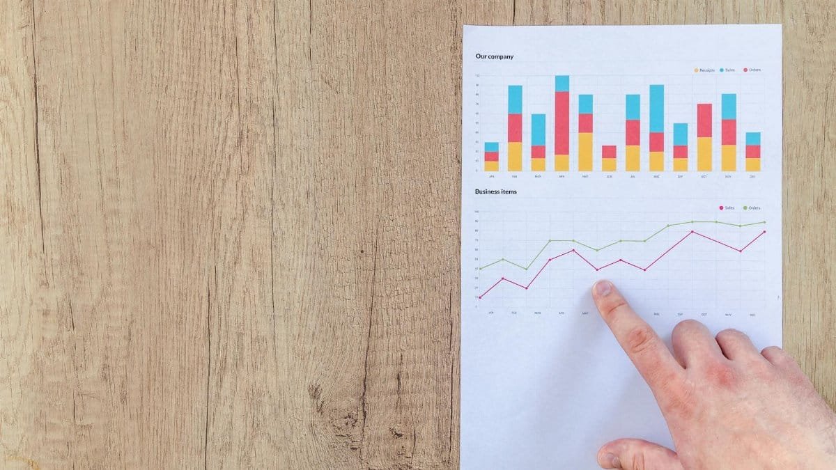 Hand analyzing business graphs on a wooden desk, focusing on data results and growth analysis.