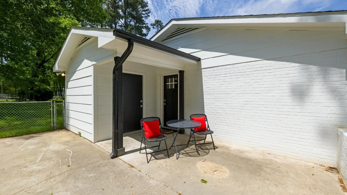 White-bricked home exterior with a small patio setup featuring black chairs and a table.