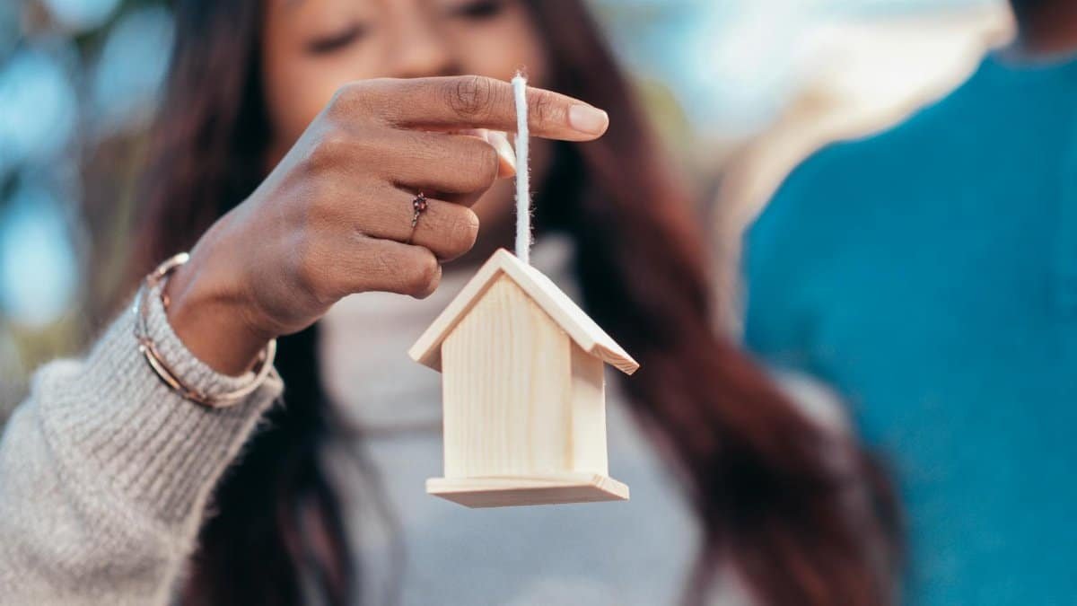 Close-up of a woman holding a wooden house symbolizing real estate or homeownership.