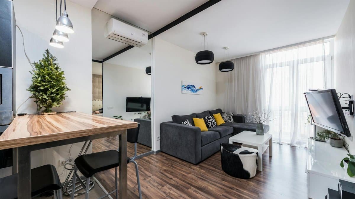 Interior of modern spacious living room with comfy sofa and wooden counter placed near big mirror reflecting TV in daytime