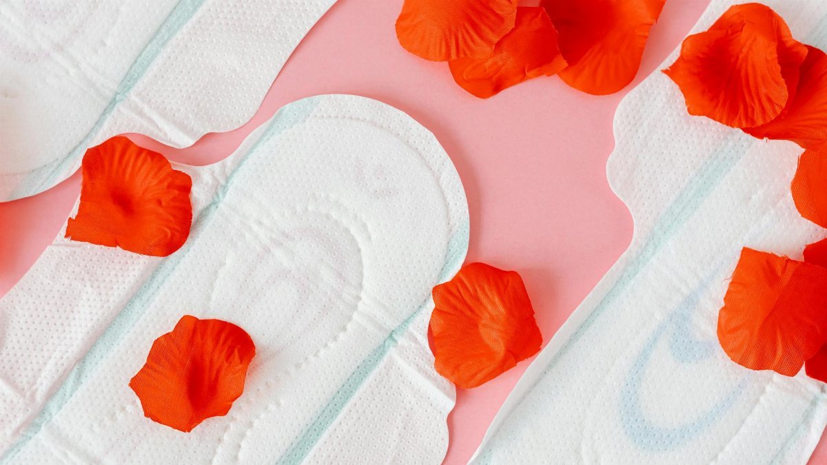 Close-up of sanitary pads with red petals on a pink background, symbolizing menstruation.