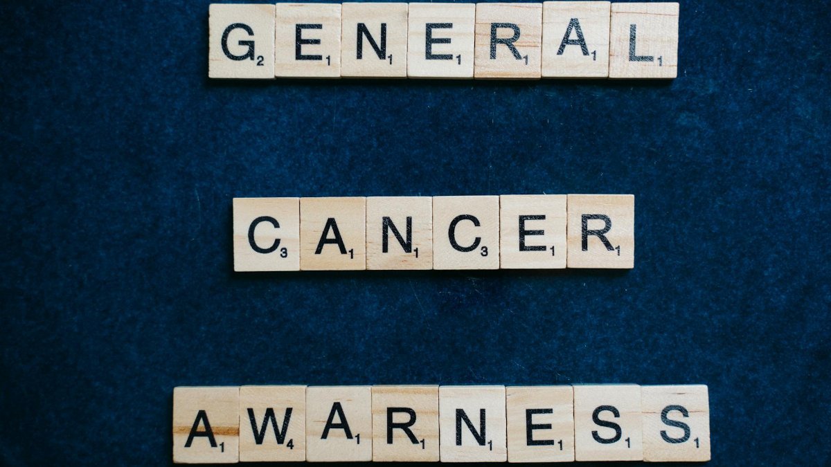 Words 'General Cancer Awareness' spelled with Scrabble tiles on a blue surface, promoting awareness.