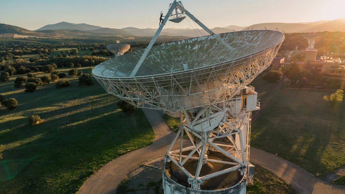 Aerial shot of a large satellite dish in a lush landscape at sunrise.