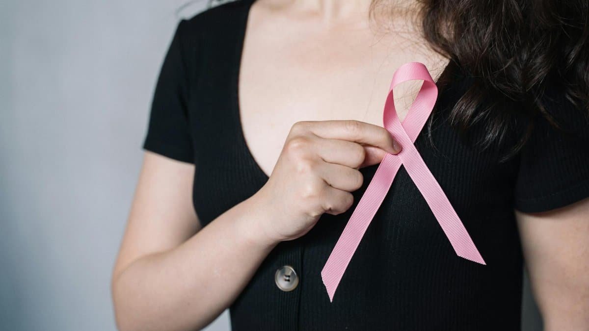Close-up of a woman holding a pink ribbon symbolizing breast cancer awareness and support.
