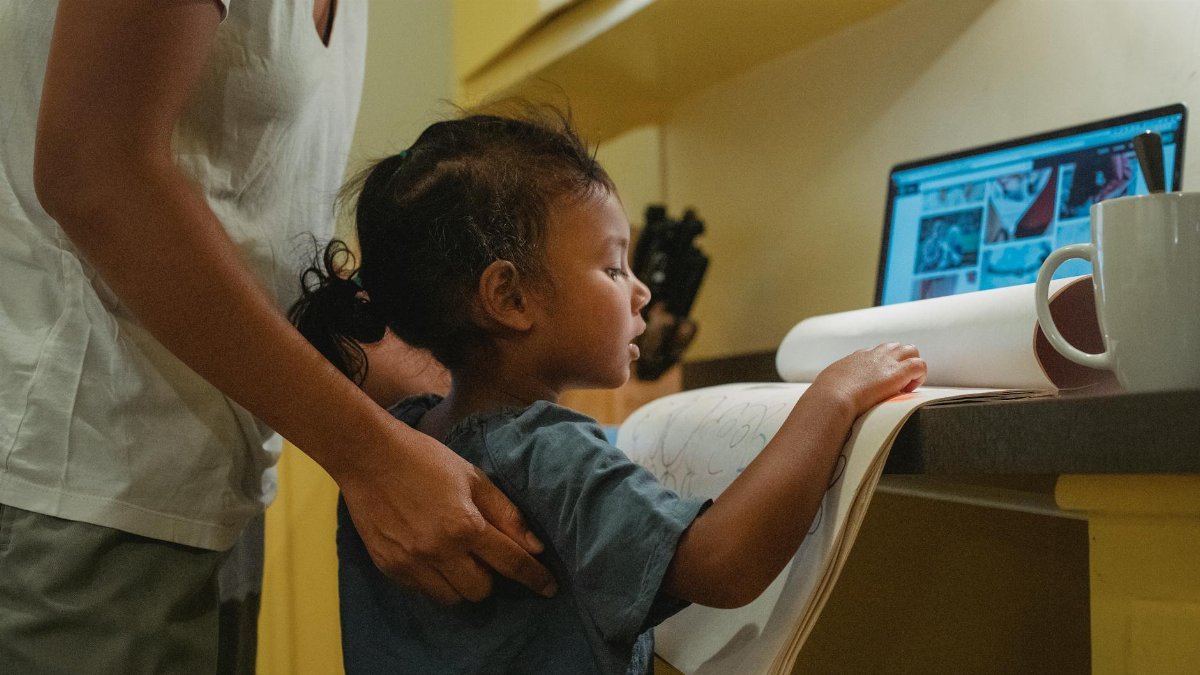 A mother assists her young child with homework at home using digital resources.