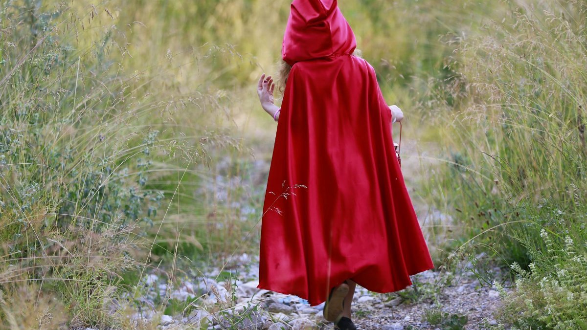 Person wearing a red cape walking in nature, evoking Little Red Riding Hood.