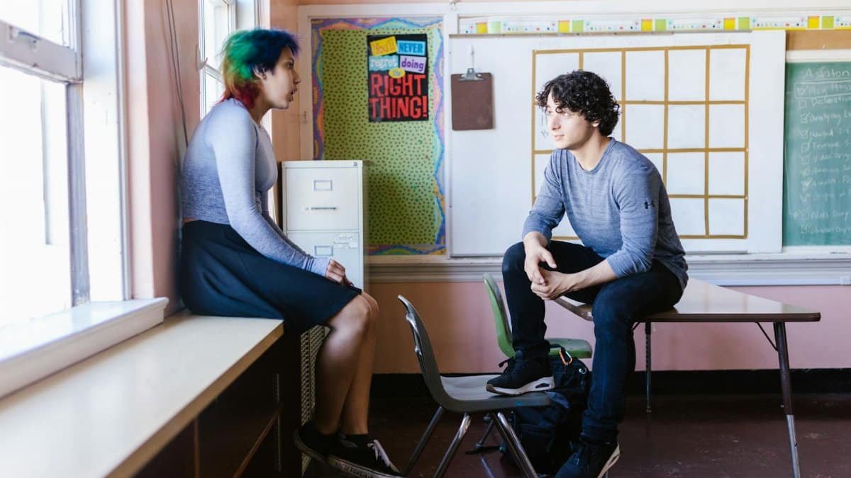Two students engaged in a conversation in a classroom setting, reflecting an educational environment.