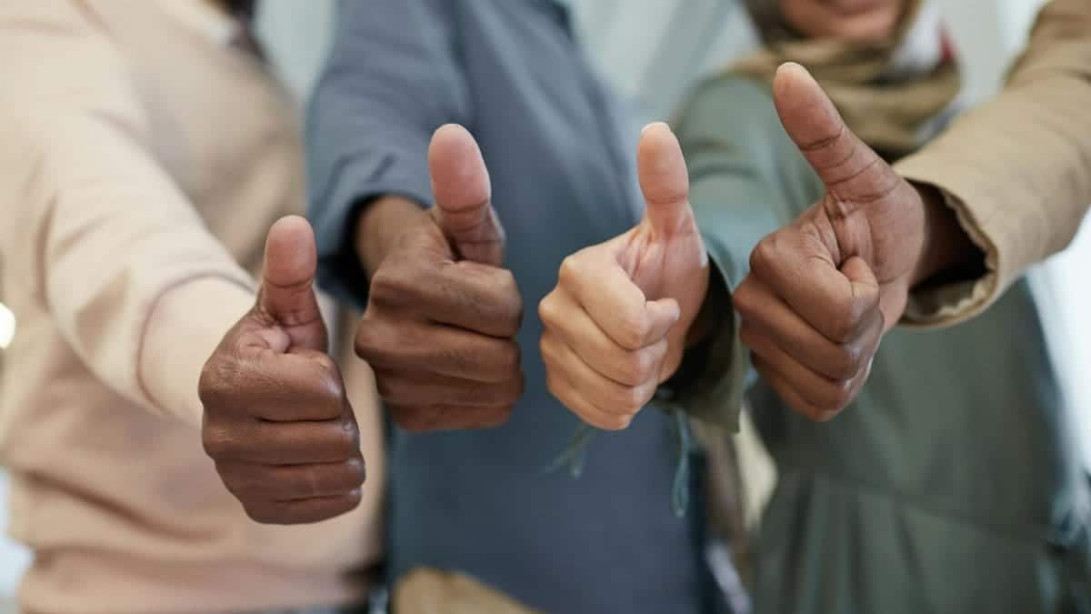 Close-up of a diverse team giving thumbs up indoors, symbolizing success and unity.